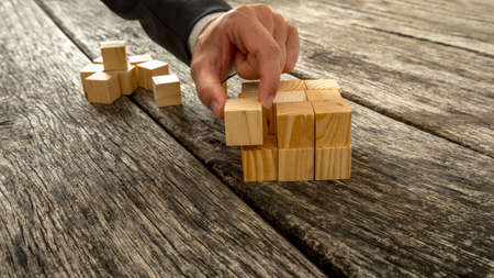 Closeup of businessman assembling blank wooden cubes into a structured whole on antique wooden desks. Conceptual of business start up, vision and strategy.