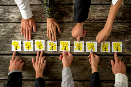 Brainstorming and teamwork concept with a group of diverse business people each holding out a card with a shining light bulb arranged in a row conceptual of ideas, inspiration and innovation.の写真素材