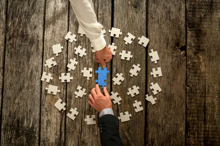 Teamwork in business concept with two businessmen around a circle of scattered white puzzle pieces...