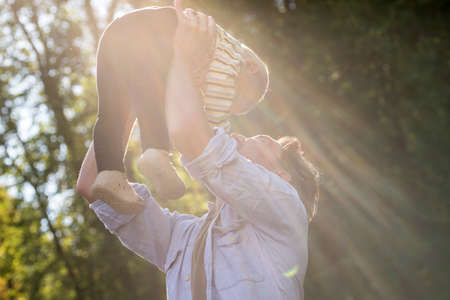 Half Body Shot of a Daddy Holding his Cute Baby Up High at the Park Early in the Morning.の写真素材