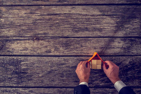 Vision of new home -  overhead view of architect or real estate agent placing a roof on top of house miniature made of many wooden cubes on textured wooden planks.の写真素材