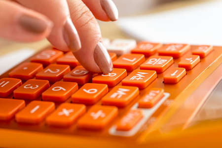 Closeup of female accountant pressing number eight on orange desktop calculator in an accounting, research or education concept.の写真素材