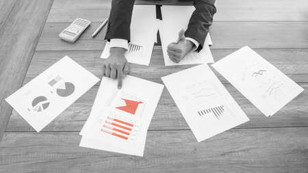 Greyscale image with selective color of a successful businessman pointing to a red chart amongst...