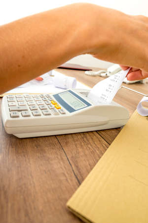 Closeup of business accountant or financial adviser making calculations using adding machine and checking numbers on receipt coming from the machine.の写真素材