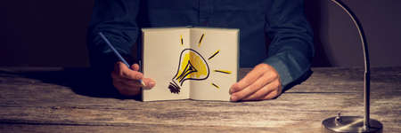 Businessman or student showing his working notebook with a hand drawn light bulb. Conceptual of innovation, idea and vision for personal and business progress.の写真素材