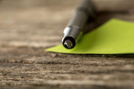 Closeup of ink pen pointing  towards you  lying on a green note paper with focus to the point of pen.の写真素材