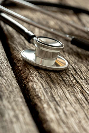 Closeup of stethoscope disc on an old rustic wooden desk.の写真素材