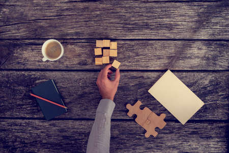 Top View of Businessman Hand Arranging Small Wooden Blocks on Rustic Table with Notes and a Cup of...