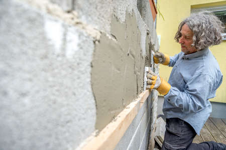 Builder applying tiles to a wall with tile cement in an architectural, renovation, DIY or new build concept, oblique angle perspective.の写真素材