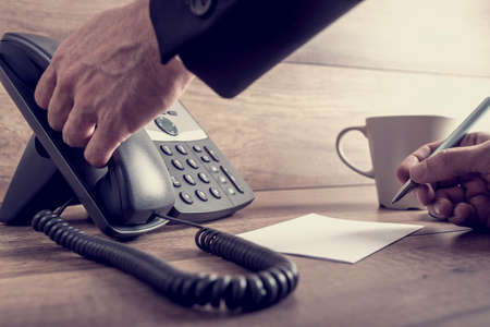 Closeup of male assistant about to answer a telephone call on black landline phone ready to take a message, with a retro filter effect.の写真素材