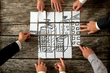 Top view of eight architects or urban planners cooperating in urban development and use of land by assembling hand drawn image of high buildings on white cards.