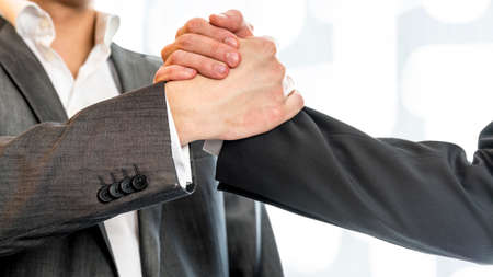 Close up of two businessmen in gray business suit gripping their hands in success and agreement at the office.の写真素材