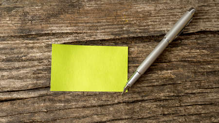 Top view of blank green card and a pen lying on a textured rustic wooden desk with copy space ready...