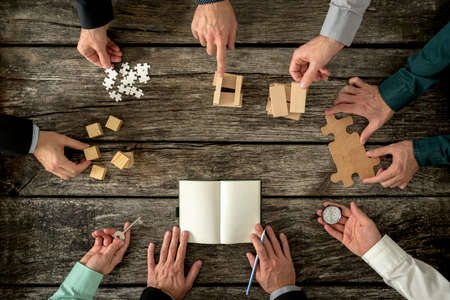 Eight businessmen planning a strategy in business advancement each holding  different but equally important metaphorical element - compass,  puzzle pieces, pegs, cubes, key and one making notes.