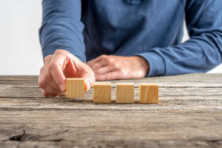 Front view of male hand placing four blank wooden cubes in a row on a textured rustic wooden desk.の写真素材
