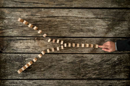Top view of businessman pushing dominos going to divide and go into two different directions. Concept of business and career opportunities.の写真素材