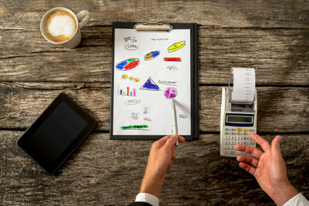 Top view of male accountant doing calculations using adding machine as he doodles various graphs, charts and calculations on a piece of paper in front of him.の写真素材