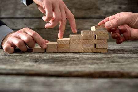 Team effort on the way to success - two male hands building stable steps with wooden pegs for the third one to walk his fingers up towards personal and career growth.