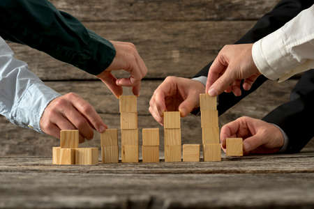 Hands of five businessman holding wooden blocks placing them into a structure. Conceptual of teamwork, strategy and business start up.の写真素材