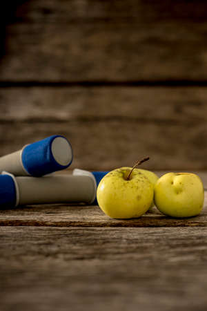 Diet and exercise concept - yellow apples and workout dumbbells on a textured wooden boards.の写真素材