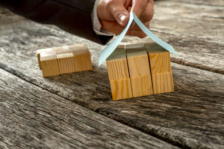 Closeup of male hand in elegant suit placing a paper roof on top of miniature house made of small wooden cubes.の写真素材