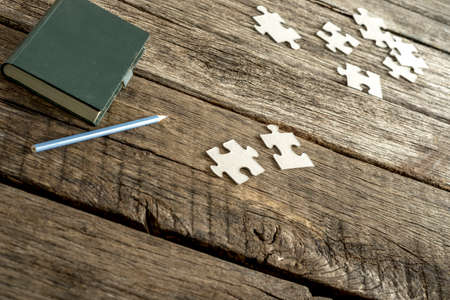 Green note pad, pencil and scattered puzzle pieces lying on a textured wooden desk. Conceptual of education, research and problem solving.の写真素材