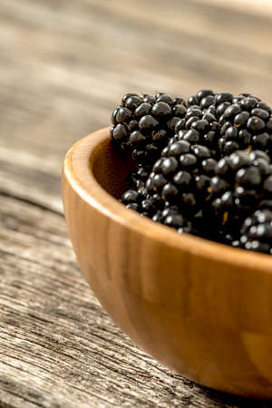 Closeup of delicious ripe blackberries heaping in a wooden bowl placed on rustic textured oak desk.の写真素材
