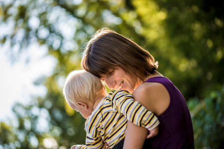 Content young mother carrying and hugging her baby boy as they enjoy a sunny day outside in nature.