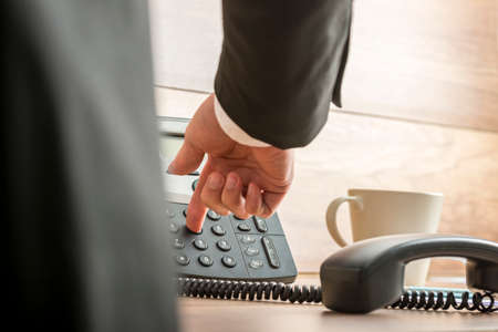 Businessman dialing telephone number on a classical black landline telephone with receiver off the...