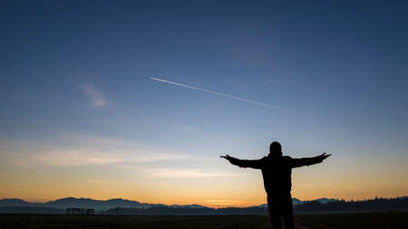 Silhouette of a man standing with his back to the camera with arms spread widely in a beautiful...
