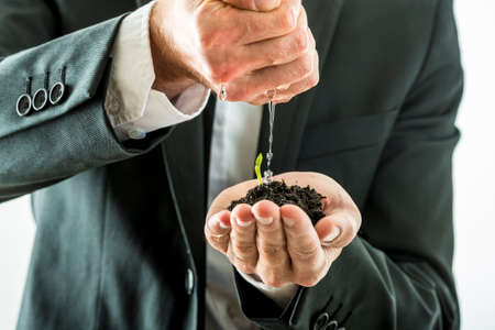Closeup of businessman watering and nurturing a green sprout growing from a fertile soil he is holding in his cupped hand. Conceptual of business vision and start up.の写真素材