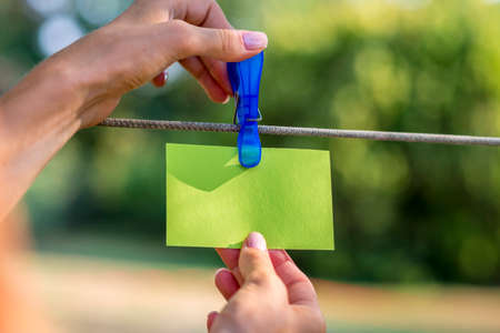 Female hand hanging a blank green card with plastic peg on a rope outside.の写真素材