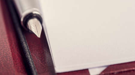 Closeup of a tip of an ink pen lying in a leather folder next to a blank piece of paper, retro effect faded look.の写真素材
