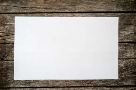 Top view of blank white piece of paper on a textured rustic wooden desk.