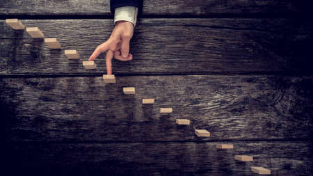 Retro image of a businessman walking his fingers up wooden steps mounted in rustic wooden boards towards light in a conceptual image of personal development, growth and success.の写真素材