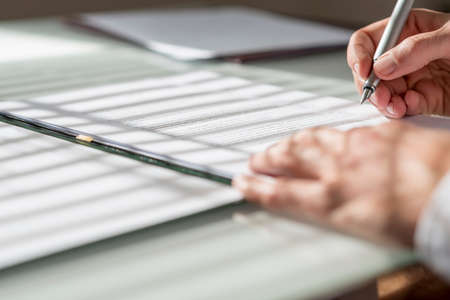Closeup low angle view of man signing a contract or document with light from the window falling on...