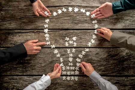 Top view of six business people, male and female, assembling a light bulb shape of small puzzle...