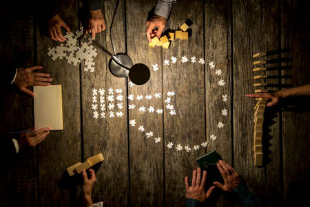 Teamwork and research concept - top view of six business people, male and female, working together on a project by using wooden pegs, dominos and cubes, making notes and matching puzzle pieces.の写真素材
