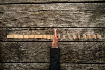 Top view of male hand in business suit stopping falling dominos on a textured wooden desk. Conceptual of crisis management.の写真素材
