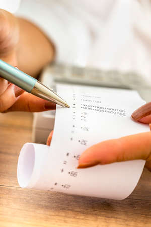 Closeup of female accountant working by checking a printout or receipt coming out of adding machine looking at numbers holding a pen.の写真素材