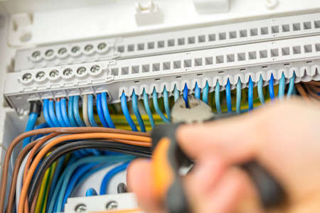 Electrician repairing faulty wiring about to clip a wire with pliers, close up of his hand, tool and...