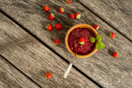 Top down view on jam in bowl with fruit over long plank on table with weathered surface.の写真素材