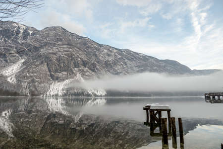 Fog rolling in on water under mountains with snow covered wooden piers in foreground with copy space.の写真素材