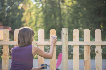 Woman varnishing a wooden picket fence outdoors in her garden in summer, retro faded effect with copy space.の写真素材