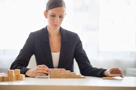 Businesswoman building a graph or ladder of success using small wooden building blocks stacked in an increasing profit and return stepped format.の写真素材