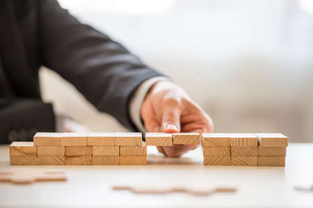 Close up of fingers from hand of business man in suit assembling a bridge made from little blocks.の写真素材