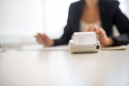 Conceptual business scene with adding machine calculator in foreground and obscured worker in...