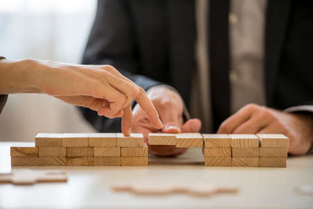 Business teamwork and cooperation concept -  male hand supporting a bridge made of wooden pegs for a female hand to walk its fingers across towards promotion and progress.の写真素材