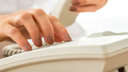 Woman with varnished nails dialling on a land line telephone instrument in a close up view conceptual of business and communication.の写真素材