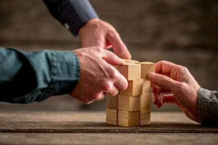 Hands of three people building a tower of wood blocks on a table, teamwork concept.